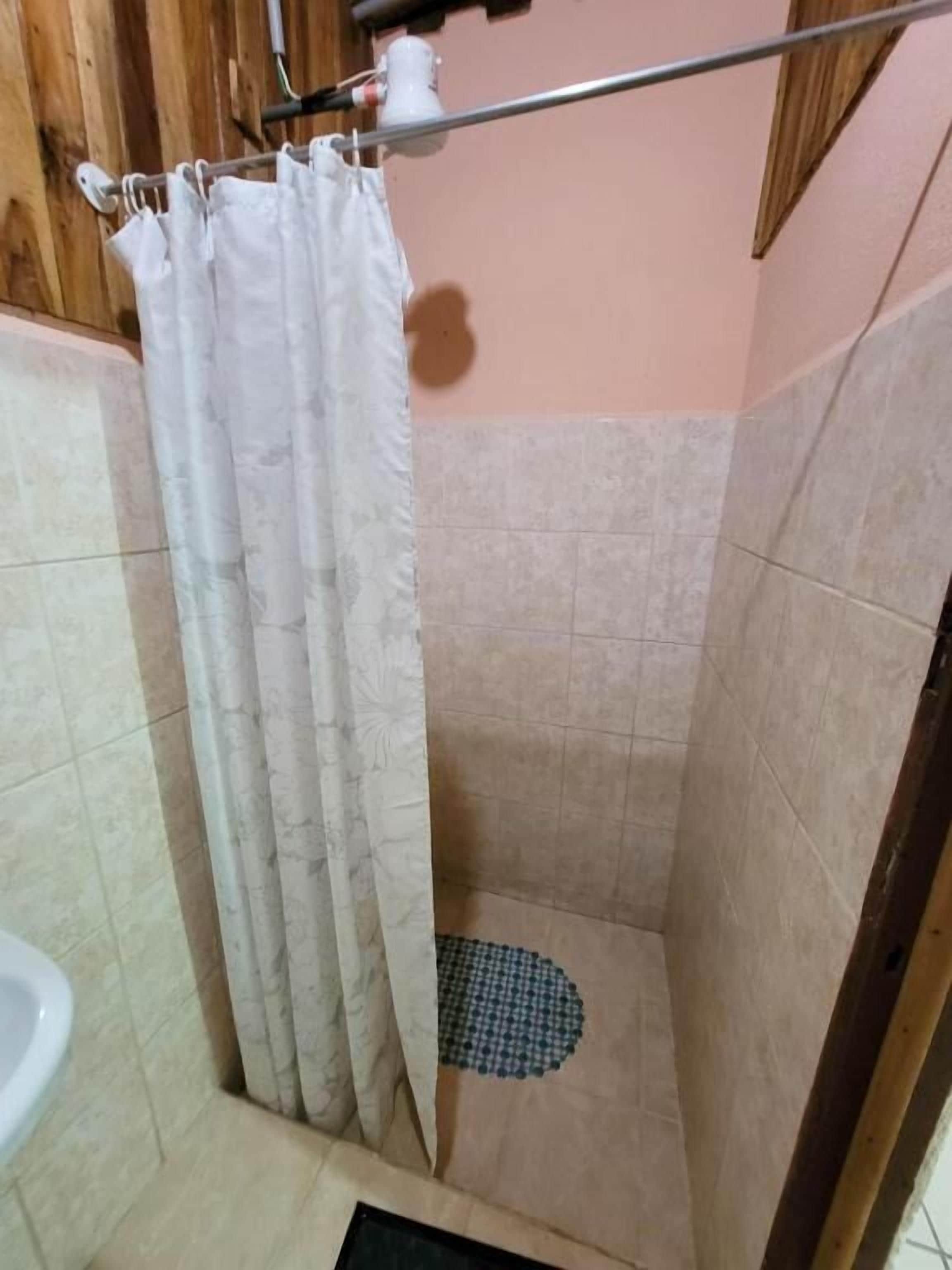 A shower area with a tiled floor, a shower curtain, and a small drain.