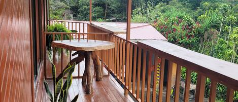 A wooden deck with a railing, potted plants, and a view of a lush, green landscape.