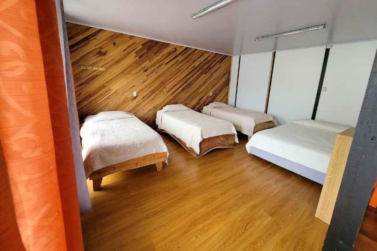 A room with three beds, wooden flooring, and a sloped ceiling with a light fixture.