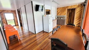 A compact kitchen with a wooden dining table and chairs, a refrigerator, and a television mounted on the wall. - Cabinas Selva Verde (Monteverde)