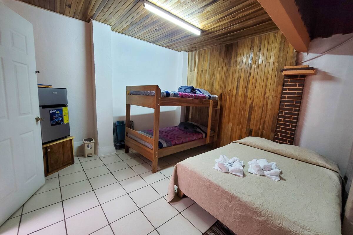 A bedroom with a bunk bed, a single bed, a refrigerator, and a suitcase.