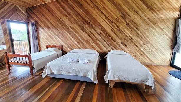 A room with two beds, wooden flooring, and a sloped ceiling. - Cabinas Selva Verde (Monteverde)