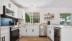 A modern kitchen with white cabinetry, stainless steel appliances, and a herringbone tile backsplash.