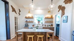 A kitchen with a central island, wooden stools, pendant lighting, and exposed brick walls. - The Isabella House: Historical, Beautifully Renovated, Walkable to Main Street

 (Buena Vista)