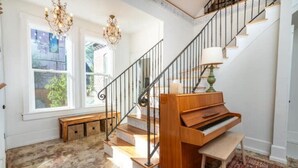 A grand staircase with a piano, chandeliers, and a bench. - The Isabella House: Historical, Beautifully Renovated, Walkable to Main Street

 (Buena Vista)