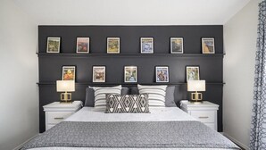 Ein aufgeräumtes Schlafzimmer mit einem großen Bett, zwei Nachttischen mit Lampen und einer Wand mit gerahmten Bildern.