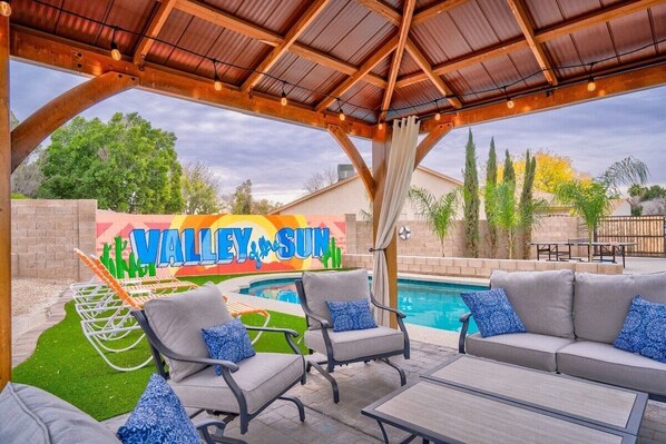 An outdoor patio area with a pool, lounge chairs, and a covered seating area.