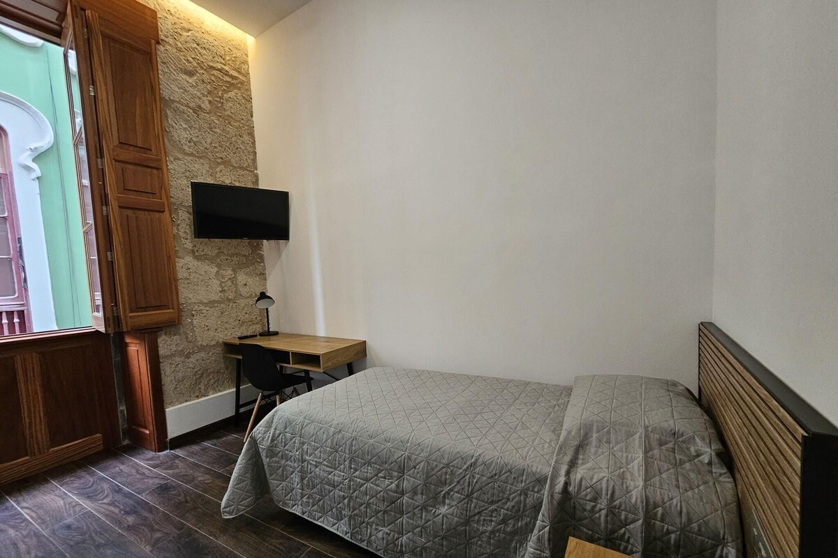 A bedroom with a bed, desk, chair, and a TV mounted on the wall.