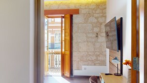 A room with a stone wall, a wooden door, a balcony with a metal railing, and a flat-screen TV mounted on the wall.