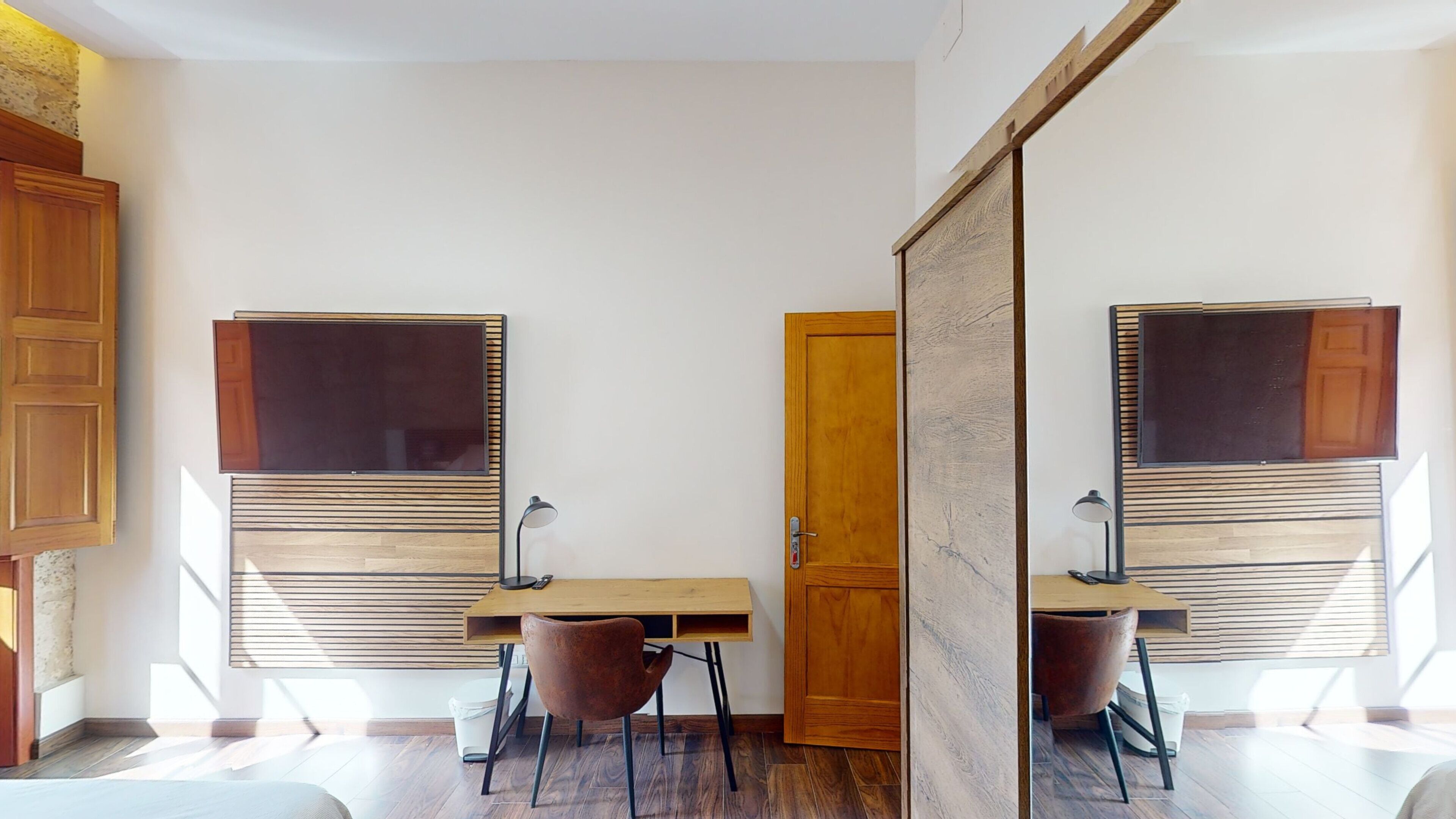 Una habitación pequeña con dos escritorios, cada uno con un televisor, una puerta y una silla.