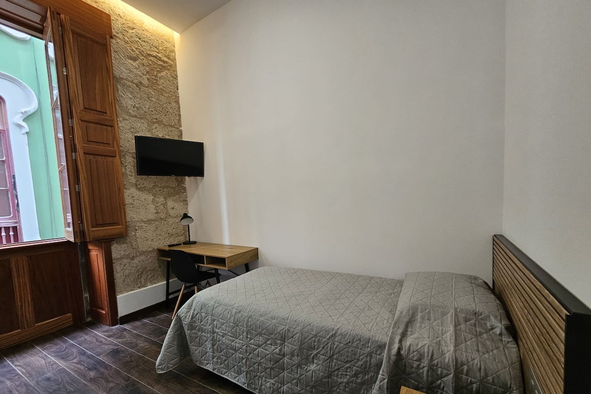 A bedroom with a bed, a desk, a chair, a television, and a stone wall.