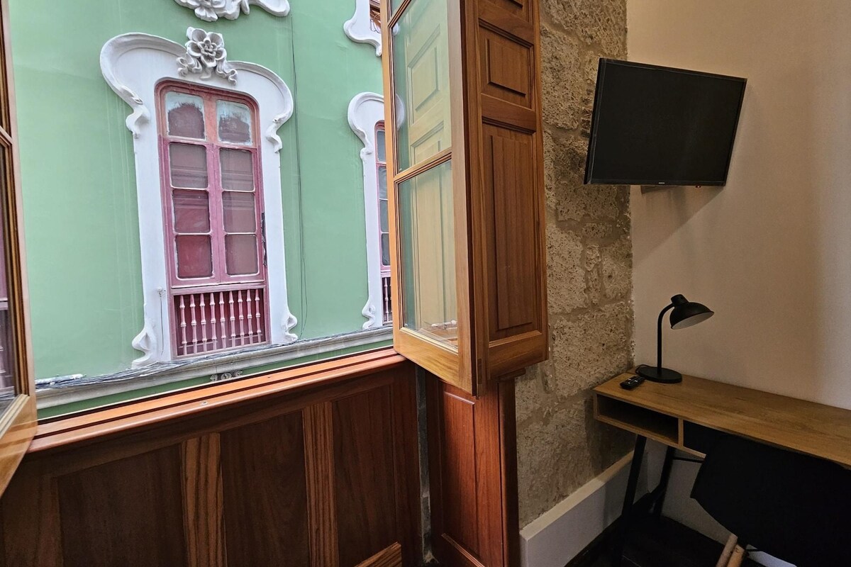 A room with a green wall, a wooden cabinet, a desk with a lamp, and a TV mounted on the wall.