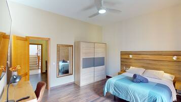 Un dormitorio con cama, mesitas de noche, armario, espejo y ventilador de techo.