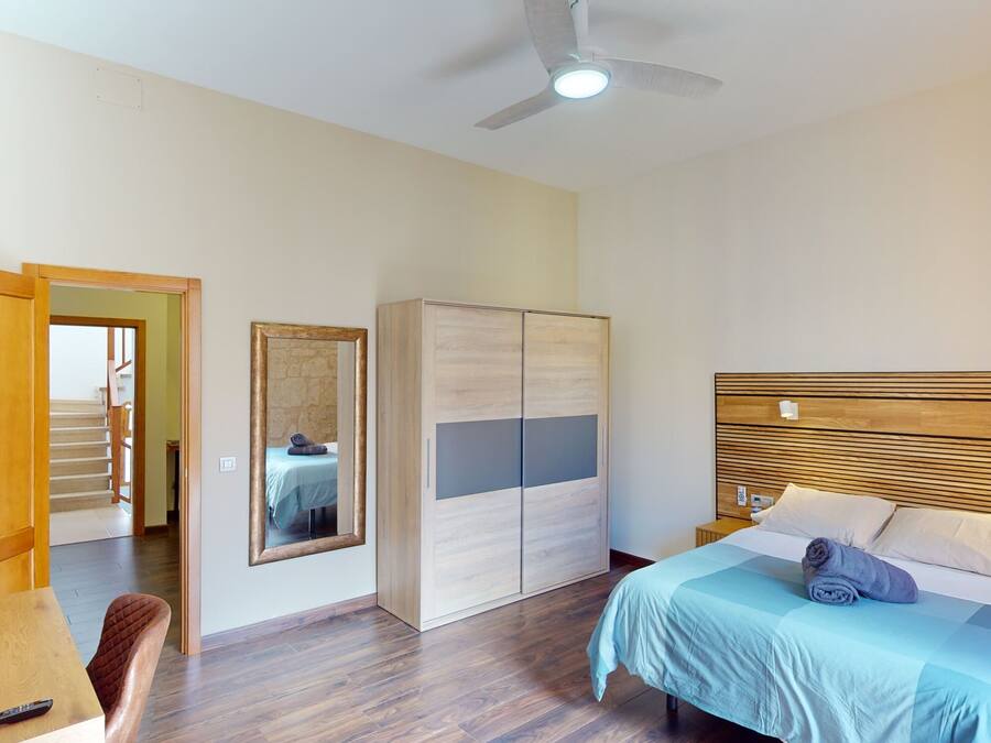 Un dormitorio con cama, mesitas de noche, armario, espejo y ventilador de techo.