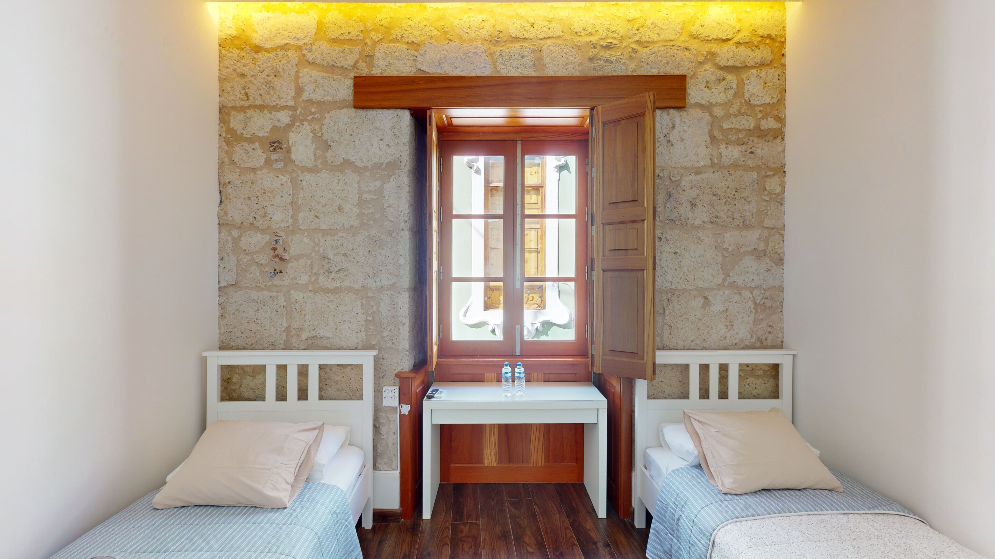 Una habitación pequeña y acogedora con dos camas individuales, un banco de madera y una ventana con vistas al exterior.