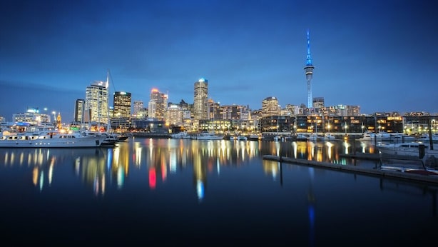 A city skyline at dusk with a prominent tower and various buildings reflected in calm water. - Stunning Auckland Harbour Views (Auckland)
