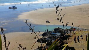 A beach with people walking, a boat, and a rocky area with water. - Stunning Auckland Harbour Views (Auckland)