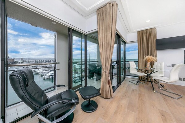 A modern room with a balcony, a glass table with chairs, and a view of the marina. - Sun Soaked Corner Apartment with Harbour View (Auckland)
