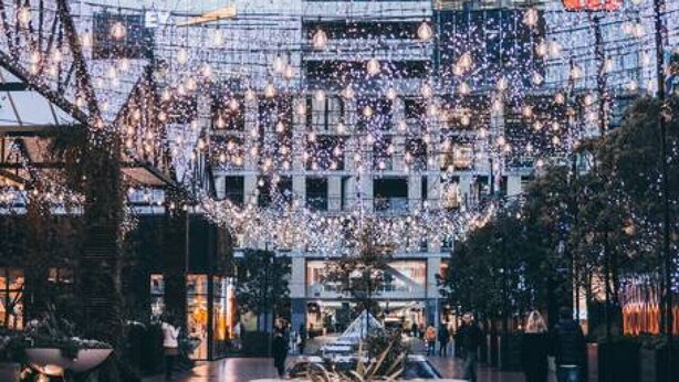 Un edificio moderno con fachada de vidrio, asientos al aire libre e iluminación decorativa.