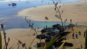 Une plage avec des gens, un bateau et des affleurements rocheux.
