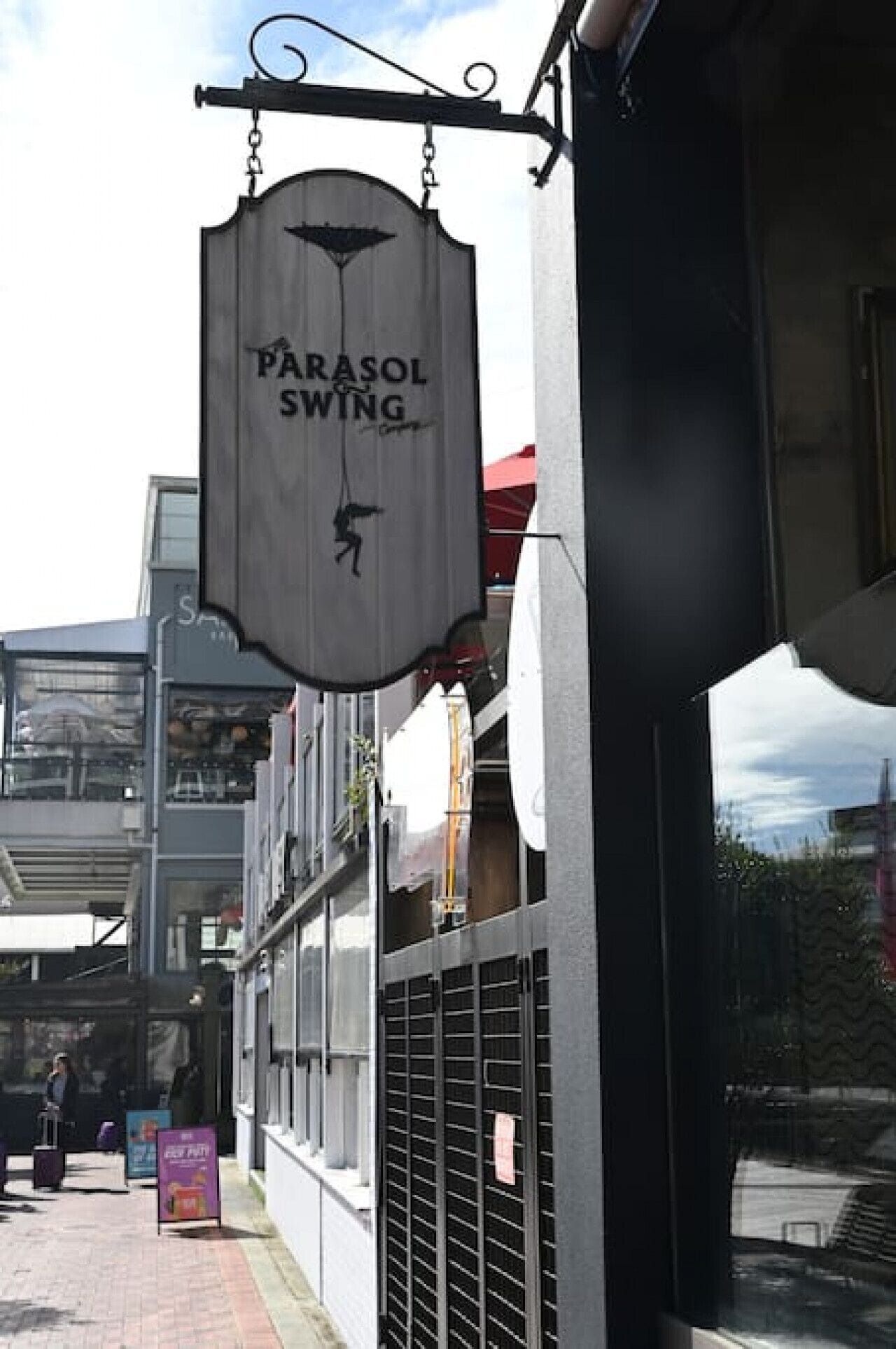 Une enseigne indiquant « PARASOL SWING » est suspendue à un bâtiment.
