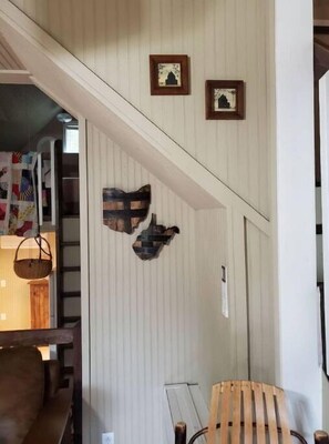 Una habitación con un banco de madera, una cesta colgante y dos cuadros en la pared.