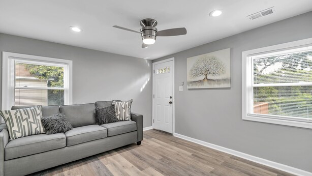 Un salon moderne avec un canapé gris, un ventilateur de plafond et un tableau représentant un arbre.