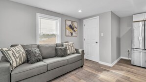 Un salon moderne avec un canapé gris, une porte blanche et un réfrigérateur en acier inoxydable.