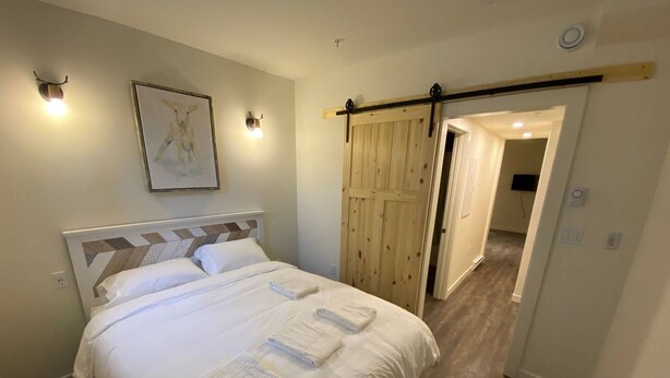 Ein Schlafzimmer mit Bett, Kopfteil, Wandbild, Schiebetür und einem Anbau.