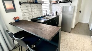 Una cocina compacta con encimera oscura, dos taburetes de bar, un microondas y un refrigerador.