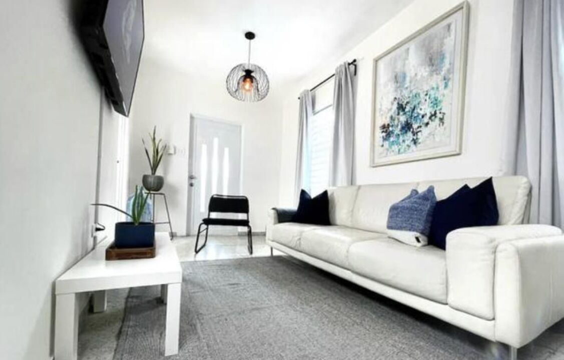 A modern living room with a white sofa, a small table, a potted plant, and a hanging light fixture.