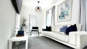 Un salón moderno con un sofá blanco, una mesita, una planta en maceta y una lámpara colgante.