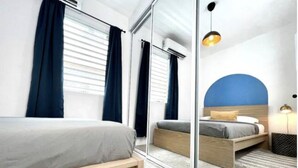 Una habitación de hotel moderna con un espejo grande, una cama con estructura de madera, una mesita de noche y una pared azul decorativa.