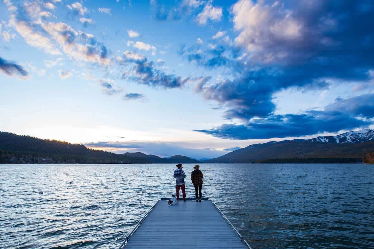 Un muelle de madera que se adentra en un lago tranquilo con montañas al fondo.
