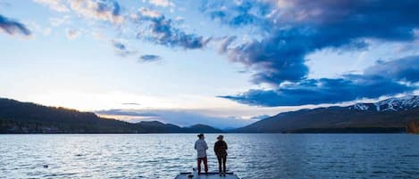 Un muelle de madera que se adentra en un lago tranquilo con montañas al fondo.