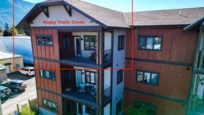 A multi-story building with balconies, labeled 'Happy Trails Condo.' - New! Beautiful Condo, Downtown Columbia Falls! (Columbia Falls)