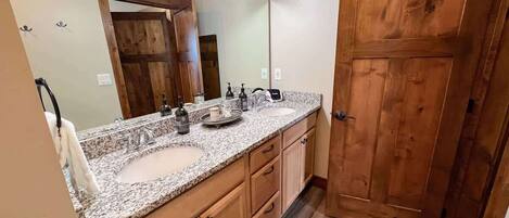 A bathroom with a double sink vanity, wooden cabinets, a large mirror, and a wooden door.