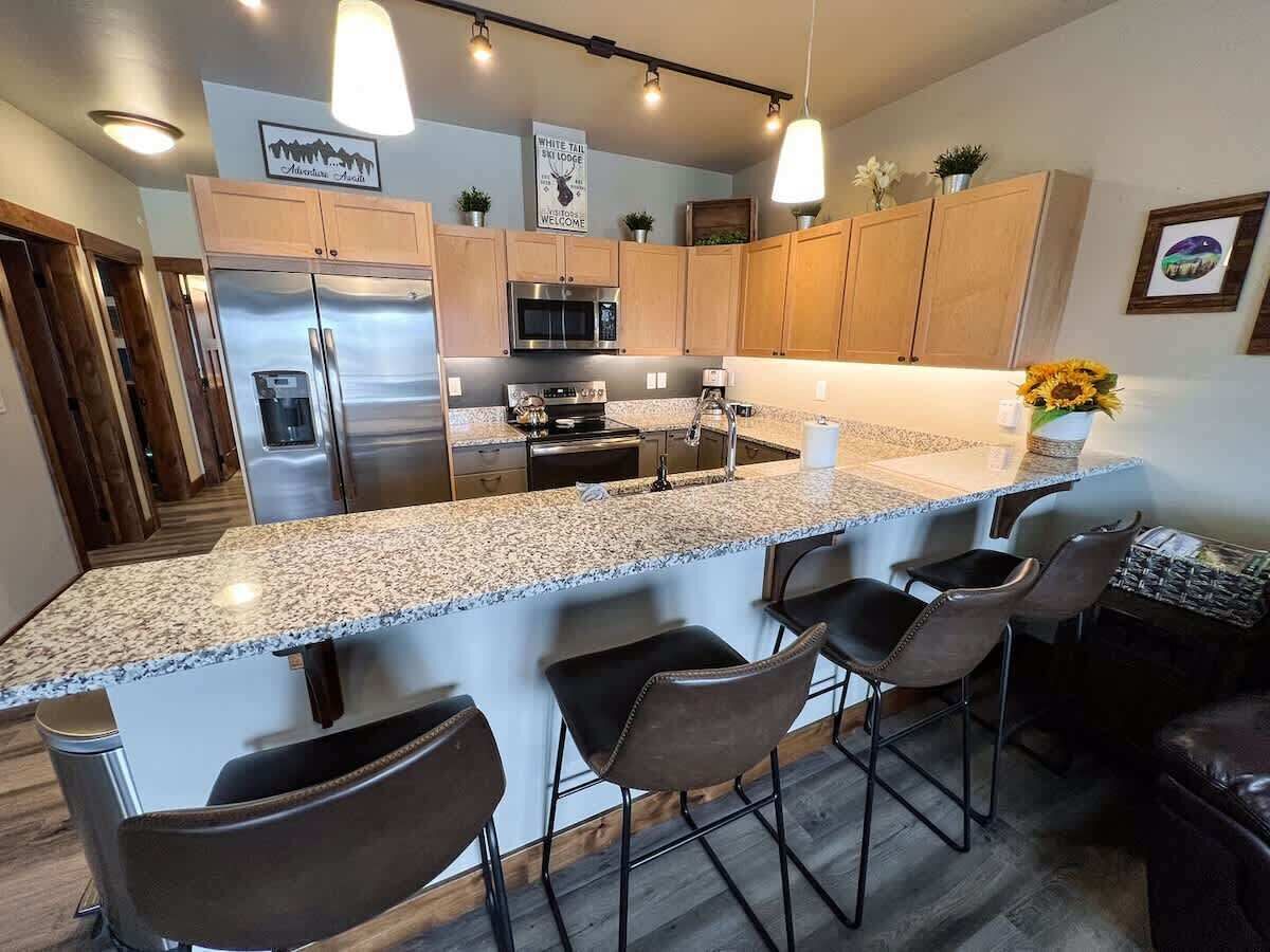 Una cocina moderna con encimeras de granito, electrodomésticos de acero inoxidable y taburetes de bar.