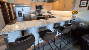 A modern kitchen with granite countertops, stainless steel appliances, and bar stools. - New! Beautiful Condo, Downtown Columbia Falls! (Columbia Falls)