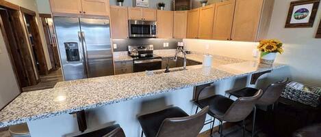 Una cocina moderna con encimeras de granito, electrodomésticos de acero inoxidable y taburetes de bar.
