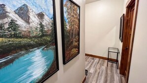 A hallway with framed landscape paintings, a small table, and wooden flooring. - New! Beautiful Condo, Downtown Columbia Falls! (Columbia Falls)