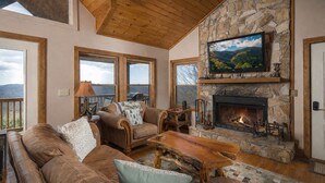 Una sala de estar acogedora con chimenea de piedra, sofás de cuero y un televisor colocado encima.