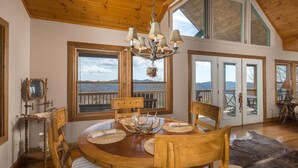 Un comedor con mesa de madera, sillas, una araña y ventanas amplias con vistas.