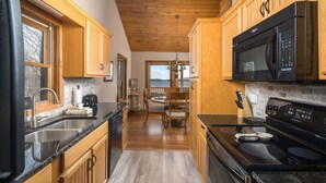 Una cocina con armarios de madera, un microondas negro, una estufa y un comedor con vistas.