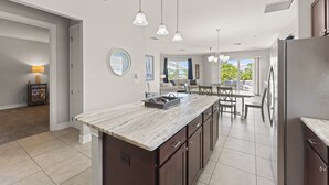 Une cuisine moderne dotée d’un plan de travail en marbre, d’appareils électroménagers en acier inoxydable et de luminaires suspendus.