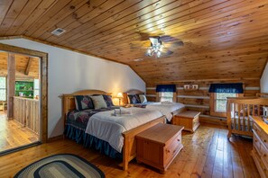Une chambre dans une cabane en rondins, avec un plafond en bois, deux lits, une table de chevet, une commode et un berceau.