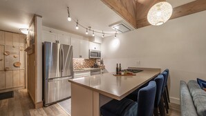 Una cocina moderna con una isla central, electrodomésticos de acero inoxidable y un comedor con sillas azules.