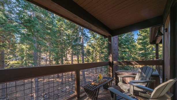 Una terraza de madera con sillas Adirondack y una mesa, con vista a un área boscosa.