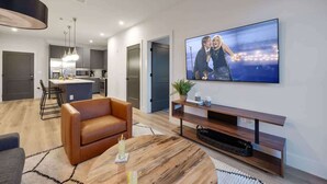 A modern living room with a flat-screen TV, a brown leather sofa, a round coffee table, and a wooden TV stand.
