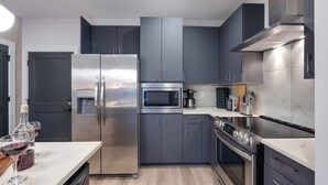 A modern kitchen with stainless steel appliances, grey cabinetry, and a marble countertop.